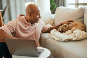 A Black man pets a dog who is curled up in a blanket on the couch