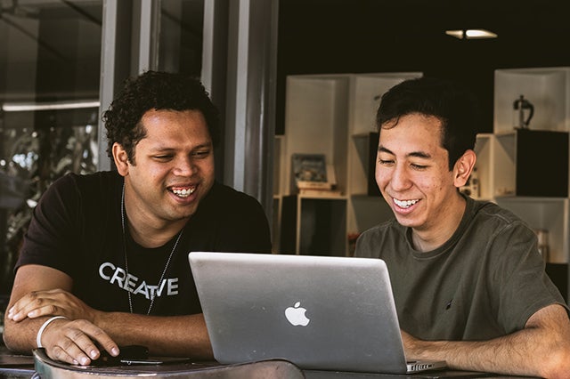 Two young BIPOC men work at laptop